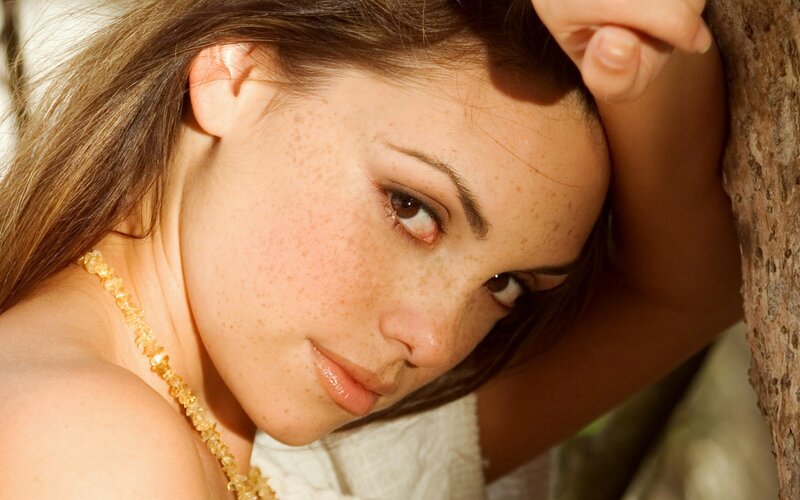 woman with freckles leaning on tree
