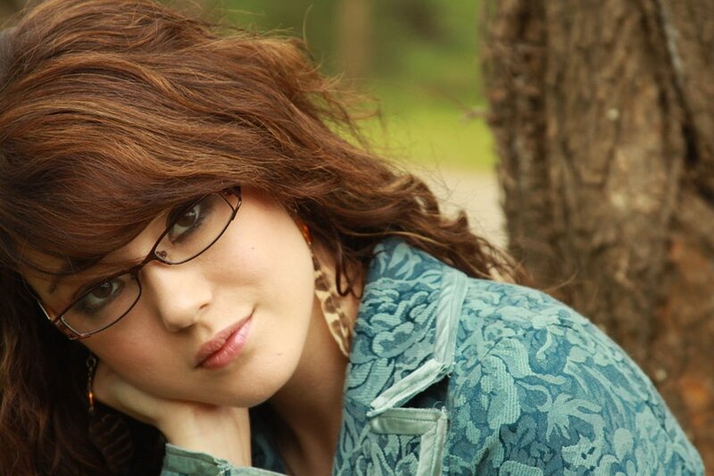woman with glasses leaning on tree