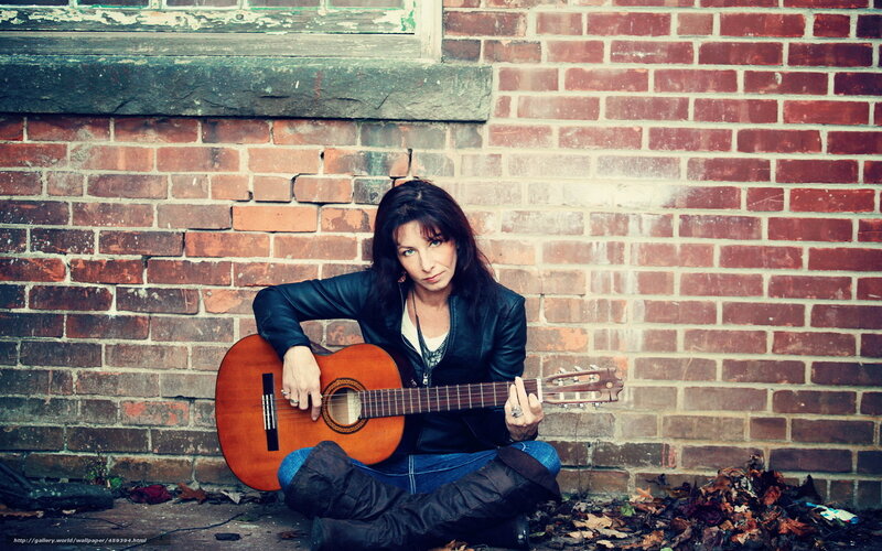 woman with guitar against brick wall