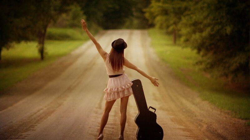 woman with guitar case on road