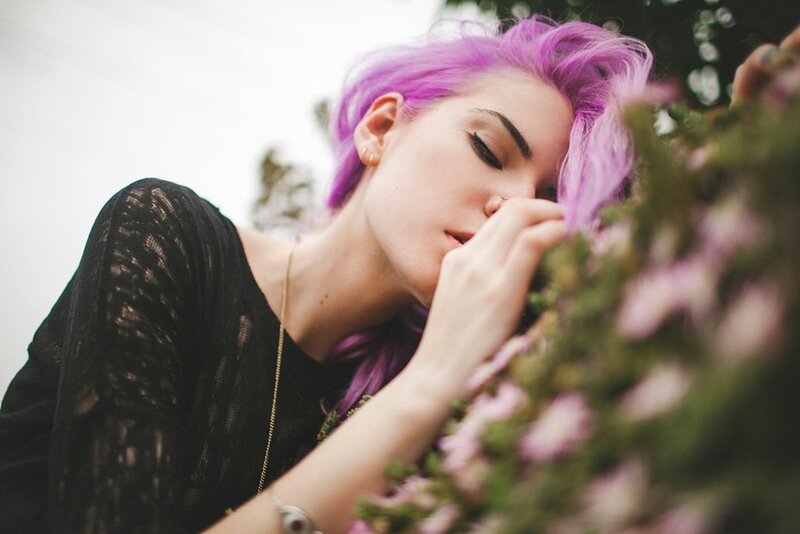 woman with purple hair smelling flowers