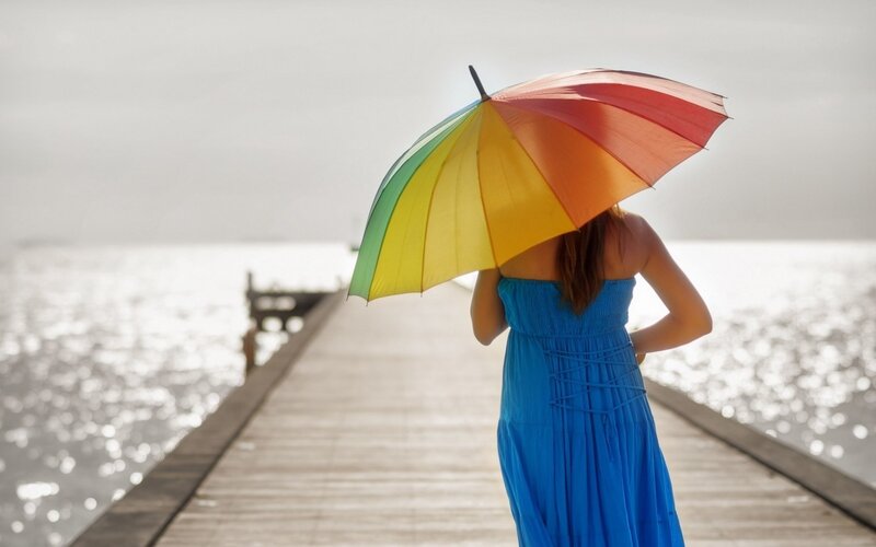 Woman with rainbow umbrella on pier
