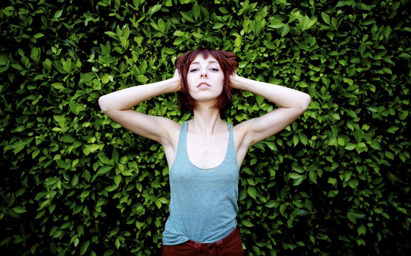 woman with red hair against green hedge