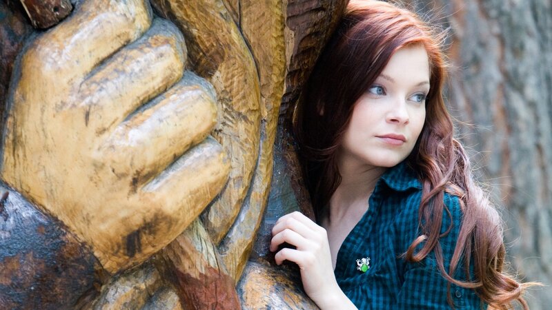 woman with red hair near wooden sculpture