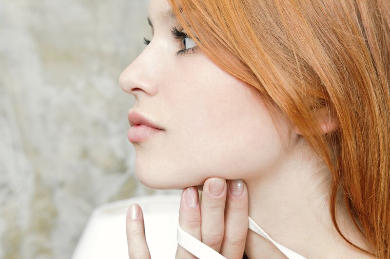 woman with red hair touching her neck