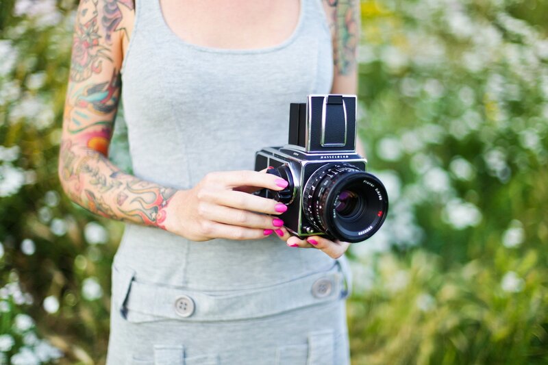 woman with tattooed arms holding camera
