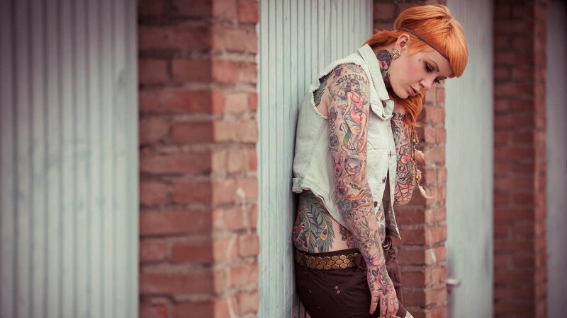 woman with tattoos leaning against wall