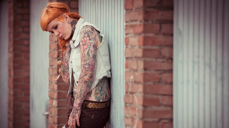 woman with tattoos leaning against wall