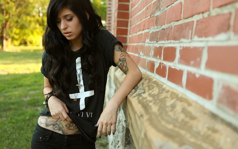 woman with tattoos leaning on brick wall