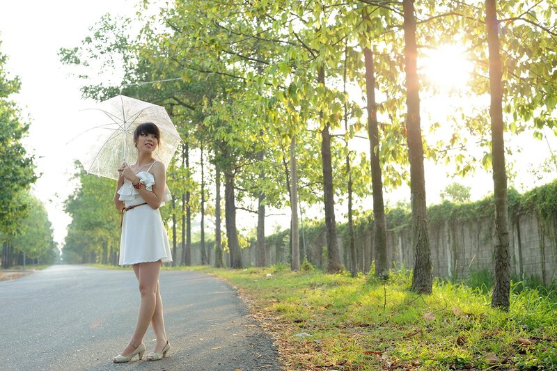 Woman with umbrella on a tree-lined road