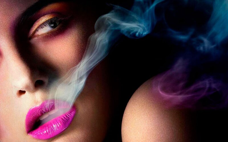 woman with vibrant makeup exhaling smoke