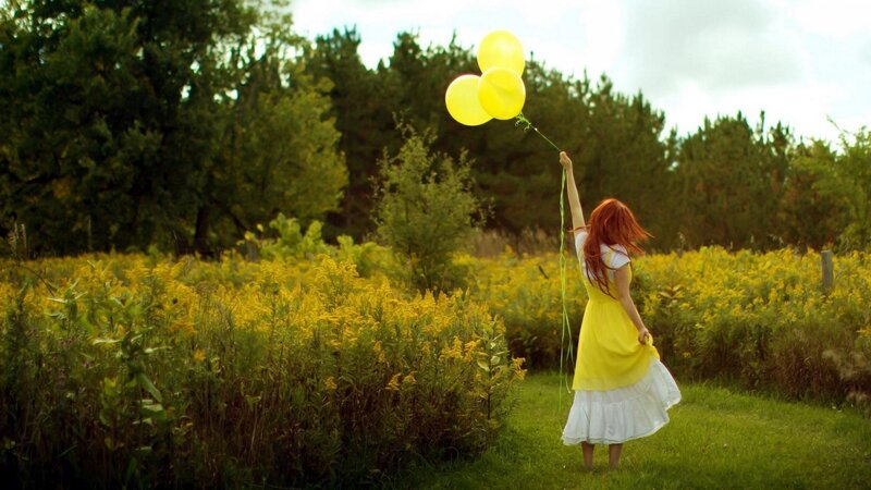 Woman with yellow balloons in field