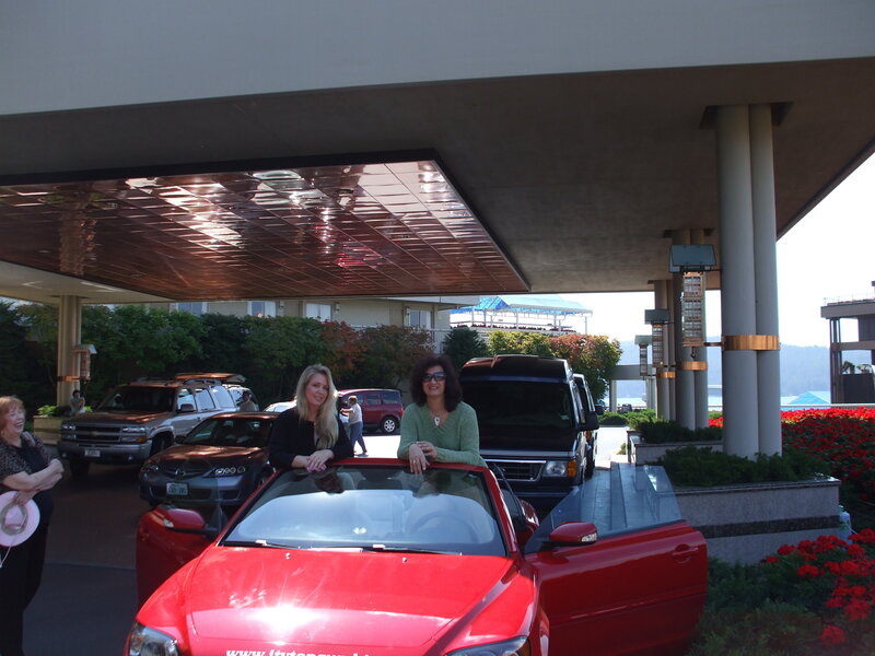 Women posing by red car at hotel