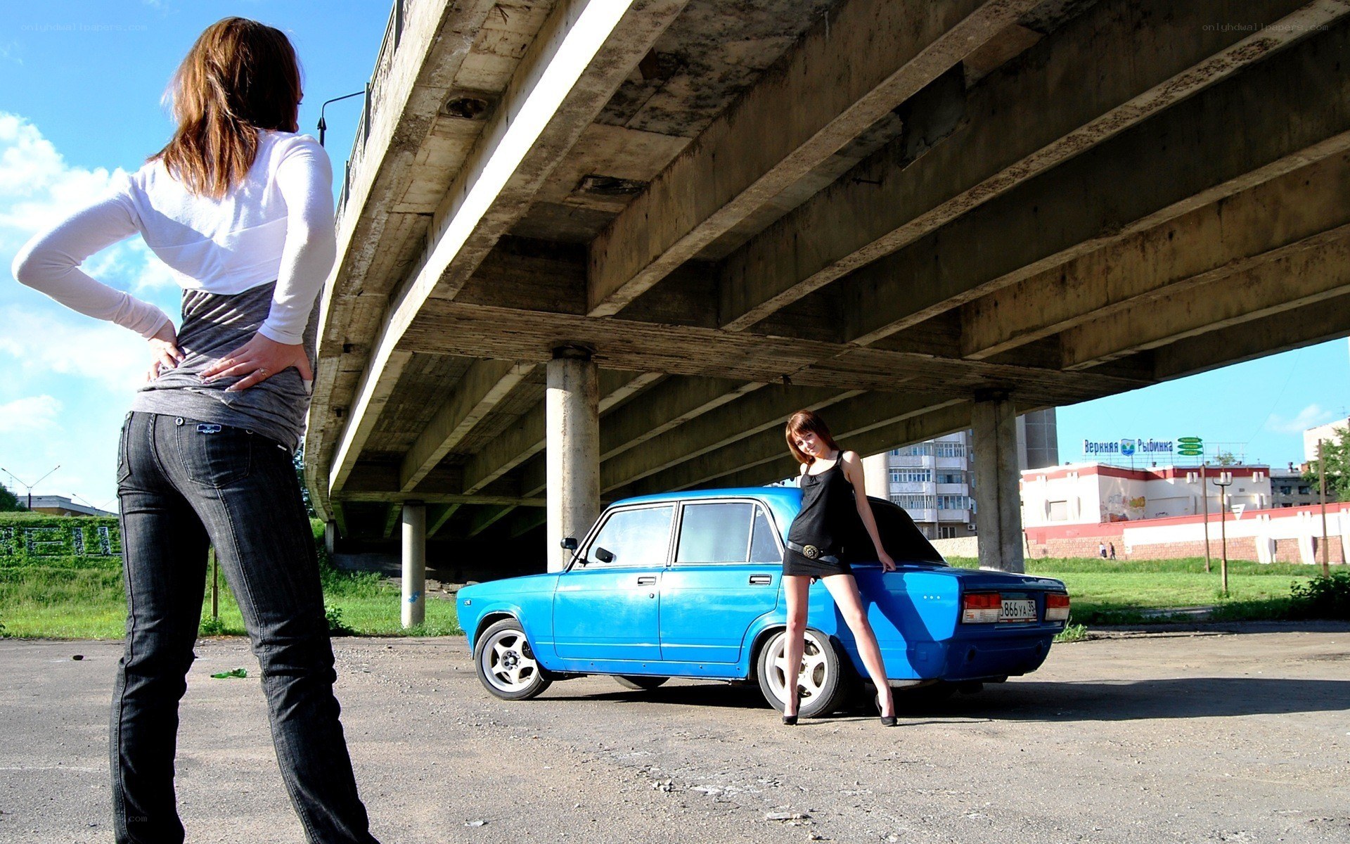 Women posing with blue car under bridge