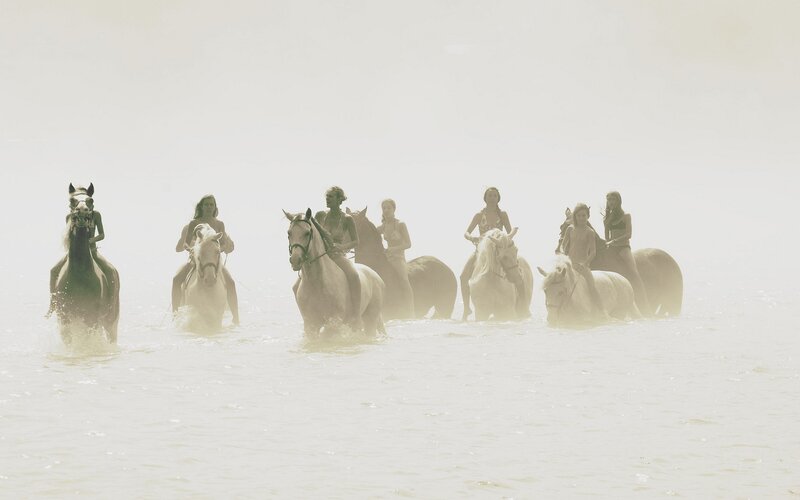 women riding horses in water
