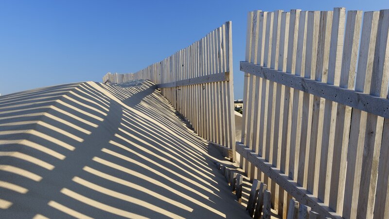 Wooden fence casting shadows on sand dune