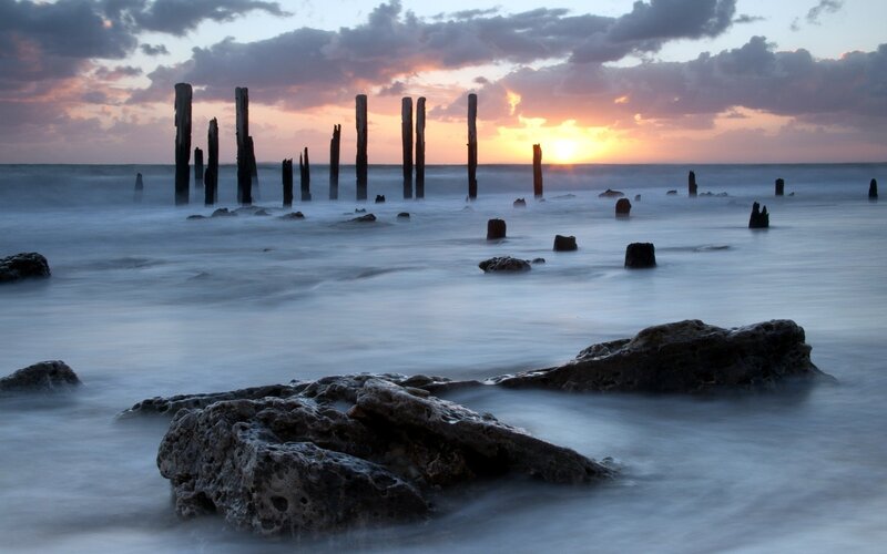 Wooden Posts in Ocean — Blue, Serene, Sunset, Photograph, Rocks, Orange, Gray