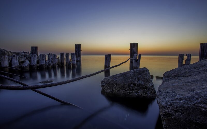 Wooden Posts in Water — Blue, Serene, Sunset, Photograph, Rocks