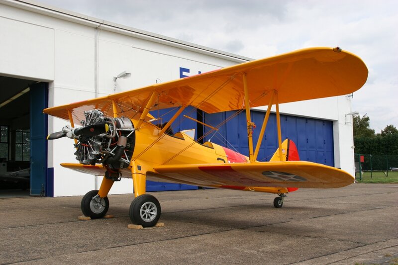 Yellow biplane in front of hangar